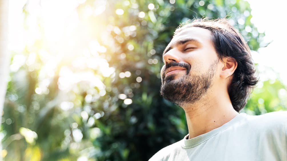 A bearded man is meditating outdoors